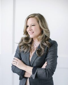 A woman in a gray suit standing with her arms crossed.